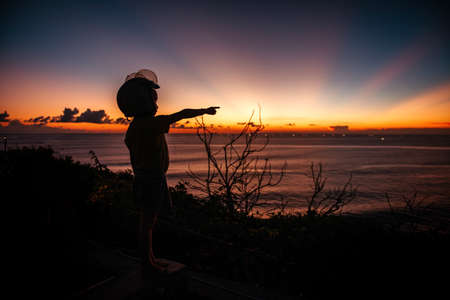 A boy in a helmet looks at the sunset at sea on the viewpoint.の写真素材
