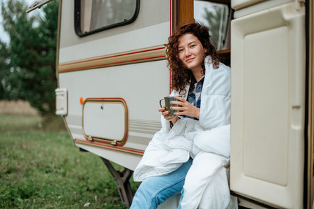 Girl sitting on the camper ladder with a mug in her hands wrapped in a blanket.