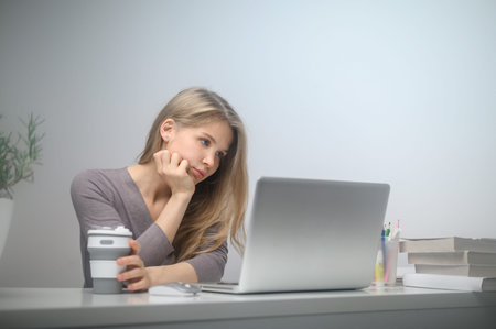 A girl with a laptop is studying at an online school. White room background