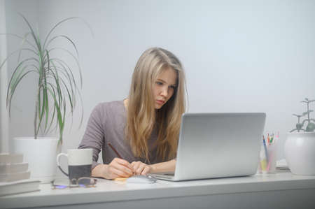 A girl with a laptop is studying at an online school. White room backgroundの写真素材