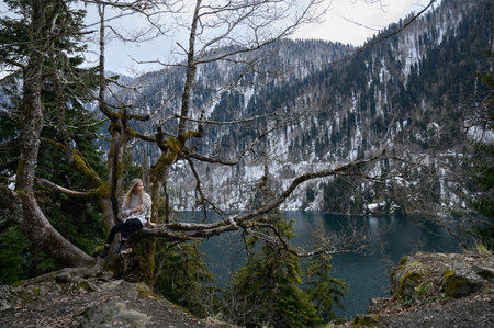 Girl sits on a tree and meditates on blue lake background. Lake Ritsa in Abkhazia