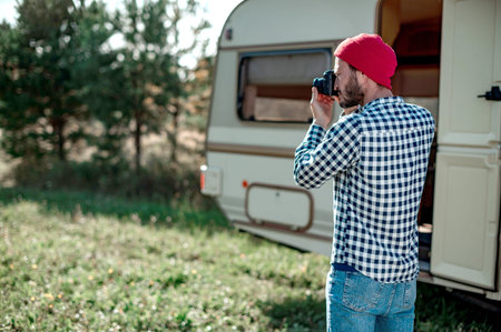 Man with a camera taking a picture in nature near the trailer at home.