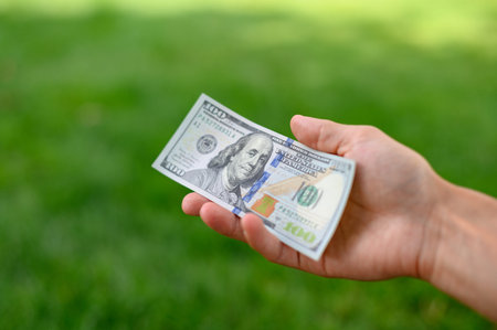 Close up 100 Dollar bank note in hand on grass background. One hundred American dollars.