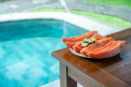 Sliced papaya with lime on table near swimming poolの写真素材