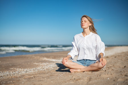 Girl meditating by the sea. Wind shakes long blond hairの写真素材