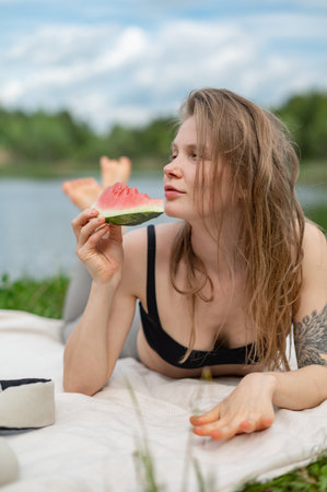 Girl relaxing and eat watermelon outdoor near lake. Picnic in natureの写真素材
