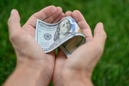 Close up 100 Dollar bank note in hand on grass background. One hundred American dollars.の写真素材