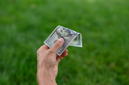 Close up 100 Dollar bank note in hand on grass background. One hundred American dollars.の写真素材