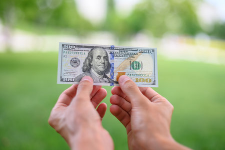 Close up 100 Dollar bank note in hand on grass background. One hundred American dollars.の写真素材