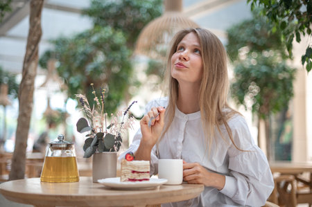 Attractive girl drinking tea with cake in cafeの写真素材