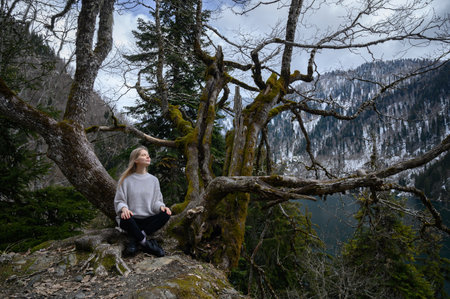 Girl sits on a tree and meditates on blue lake background.の写真素材