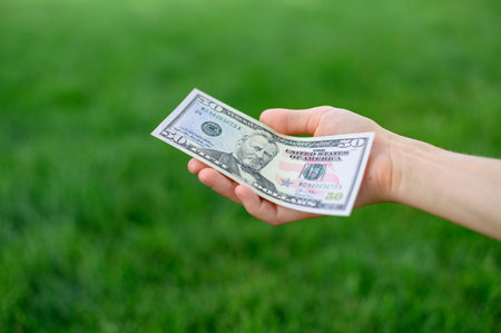 First person top view photo of hands holding fan of Dollar banknotes on park backgroundの写真素材