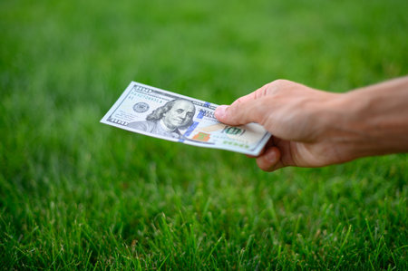 First person top view photo of hands holding fan of Dollar banknotes on park backgroundの写真素材