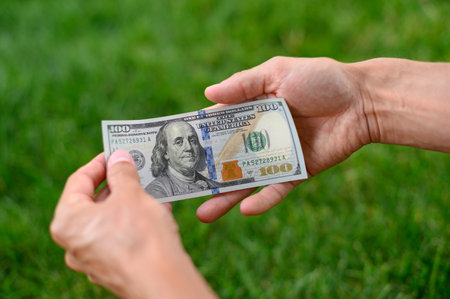 Close up 100 Dollar bank note in hand on grass background. One hundred American dollars.の写真素材