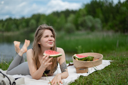 Girl relaxing and eat watermelon outdoor near lake. Picnic in natureの写真素材