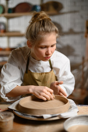 A ceramist makes a plate. Woman in an apron works in a pottery workshop.の写真素材