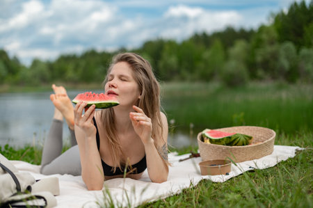 Girl relaxing and eat watermelon outdoor near lake. Picnic in natureの写真素材
