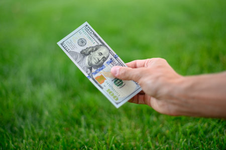 First person top view photo of hands holding fan of Dollar banknotes on park backgroundの写真素材