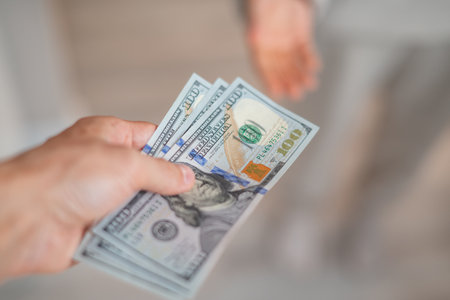 A hand passes hundred dollar bills to another personの写真素材