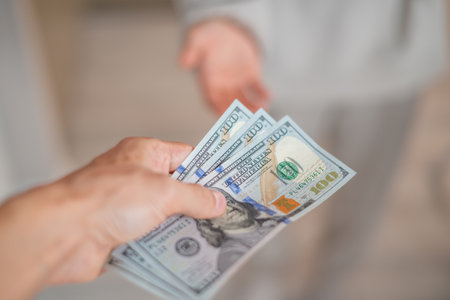 A hand passes hundred dollar bills to another personの写真素材