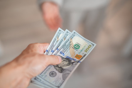 A hand passes hundred dollar bills to another personの写真素材