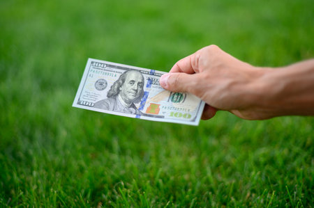 Close up 100 Dollar bank note in hand on grass background. One hundred American dollars.の写真素材
