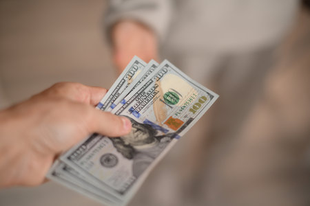 A hand passes hundred dollar bills to another personの写真素材