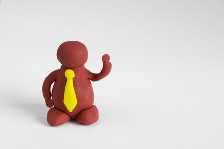 Plasticine man with a yellow tie keeping one hand up over grey backgroundの写真素材