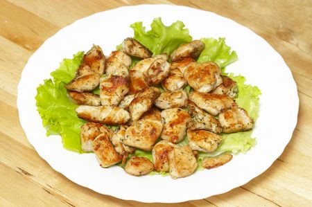 Roasted chicken pieces and leafs of salad over whtie plateの写真素材