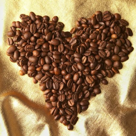 Roasted coffee grains background macro shot over golden cloth heart shapeの写真素材