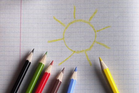 Colorful pencils set macro shot over checked paper background and sun iconの写真素材