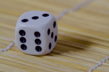 close up of a white six sided die with doted numbers on pale brown straw floor