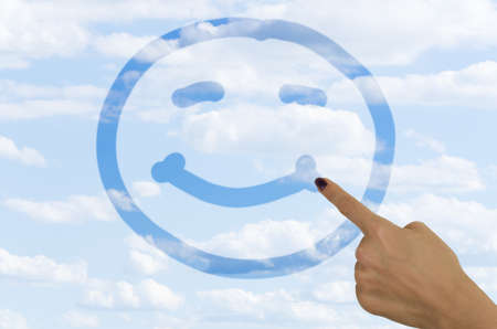 hand drawing a smiley face on a foggy window with a finger revealing clear blue sky on the other sideの写真素材