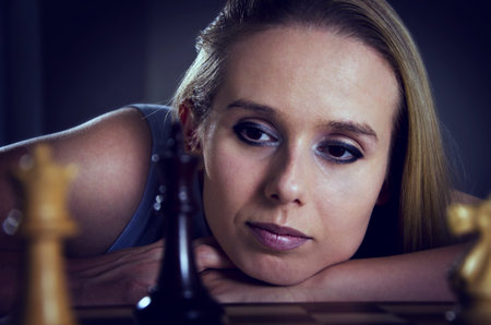 woman playing chess leaning on her arm thinking about her next moveの写真素材