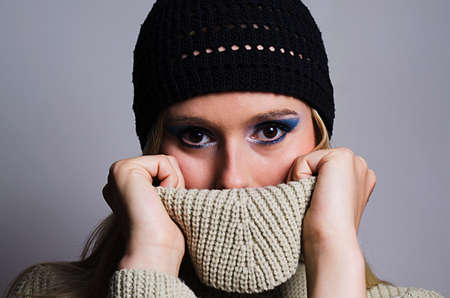 blonde woman wearing a black knitted hat covering her face with turtleneck sweaterの写真素材