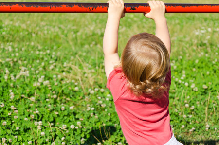 child playing in a park grabbing a red metal railing and hanging from it