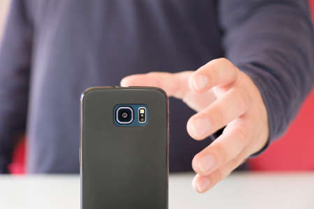 male hand reaching for a black smartphoneの写真素材