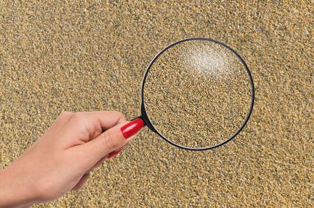 hand holding a magnifying glass enlarging grains of sand and bringing them in to focusの写真素材