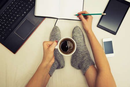woman holding a cup of coffee taking a break from work on bed surrounded by multiple communication devicesの写真素材