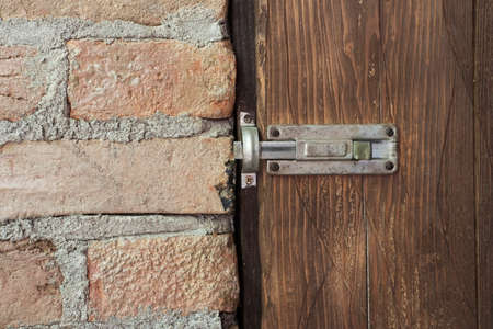 Old rusty bolt on an old wooden door connecting on to brick wallの写真素材
