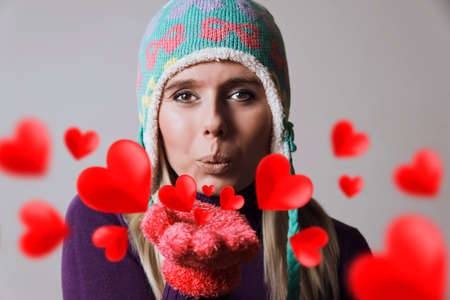 beautiful blonde woman wearing winter clothing blowing heart kissesの写真素材