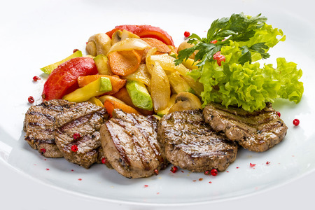 Medallions of veal with vegetables and salad. On a white plate