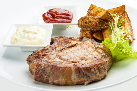 Steak from pork chop with potatoes on a white plate. With sauce red and whiteの写真素材