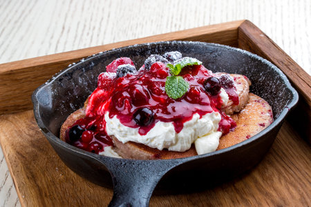 Breakfast in a pan on a white background. Pancakes with cream and jam. On a wooden tray.の写真素材