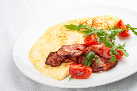 Omelet with bacon and tomatoes on white background