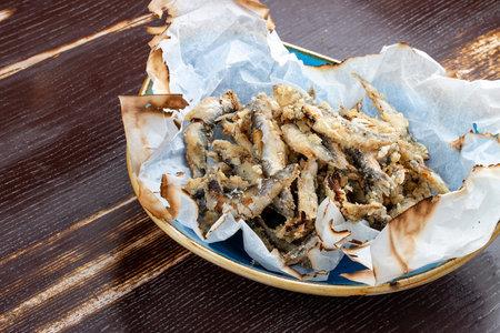 Fried sprat in parchment on wooden background
