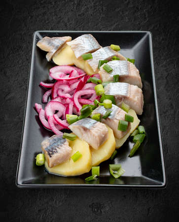 Appetizer with lightly salted herring, boiled potatoes and onions. Isolated on a black backgroundの写真素材
