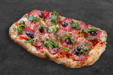 Pizza Diavolo with chorizo, rucola, jalapeno, chili, kalamata, pesto. Roman pizza rectangular on dark backgroundの写真素材