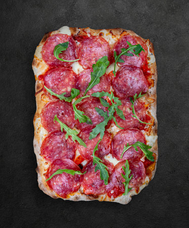 Salami pizza, bell pepper, rucola, kalamata, pesto, parmesan. Roman pizza rectangular on wood backgroundの写真素材