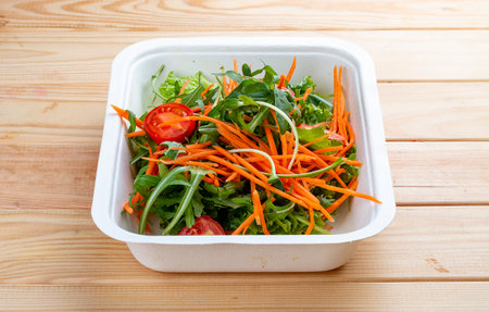 Salad mix (greens, carrots and cherry tomatoes). Healthy food. Takeaway food. On a wooden background.の写真素材